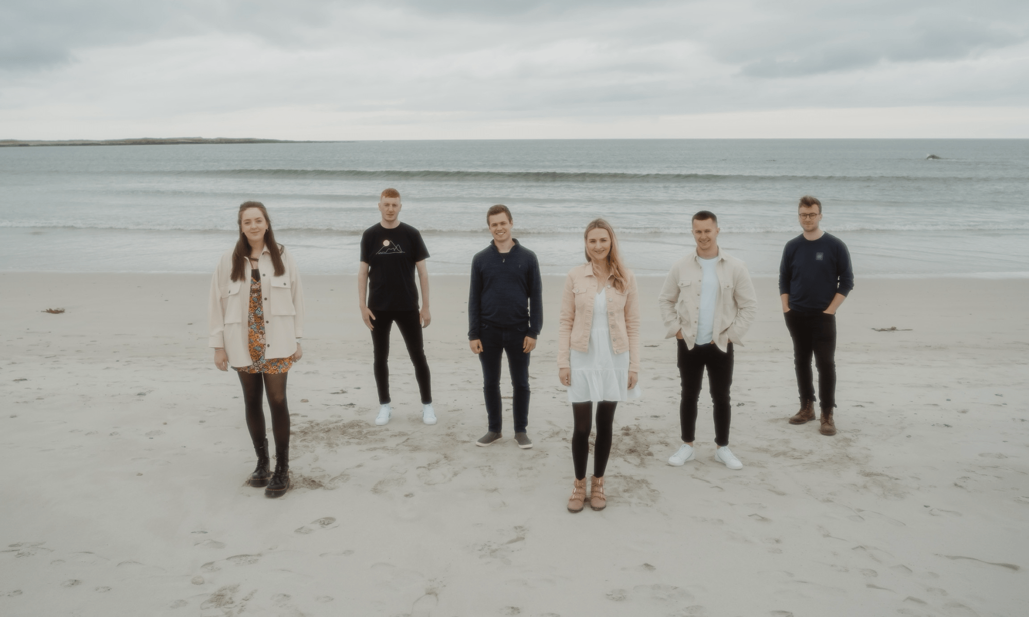 Band standing apart on white sandy beach with sea behind them